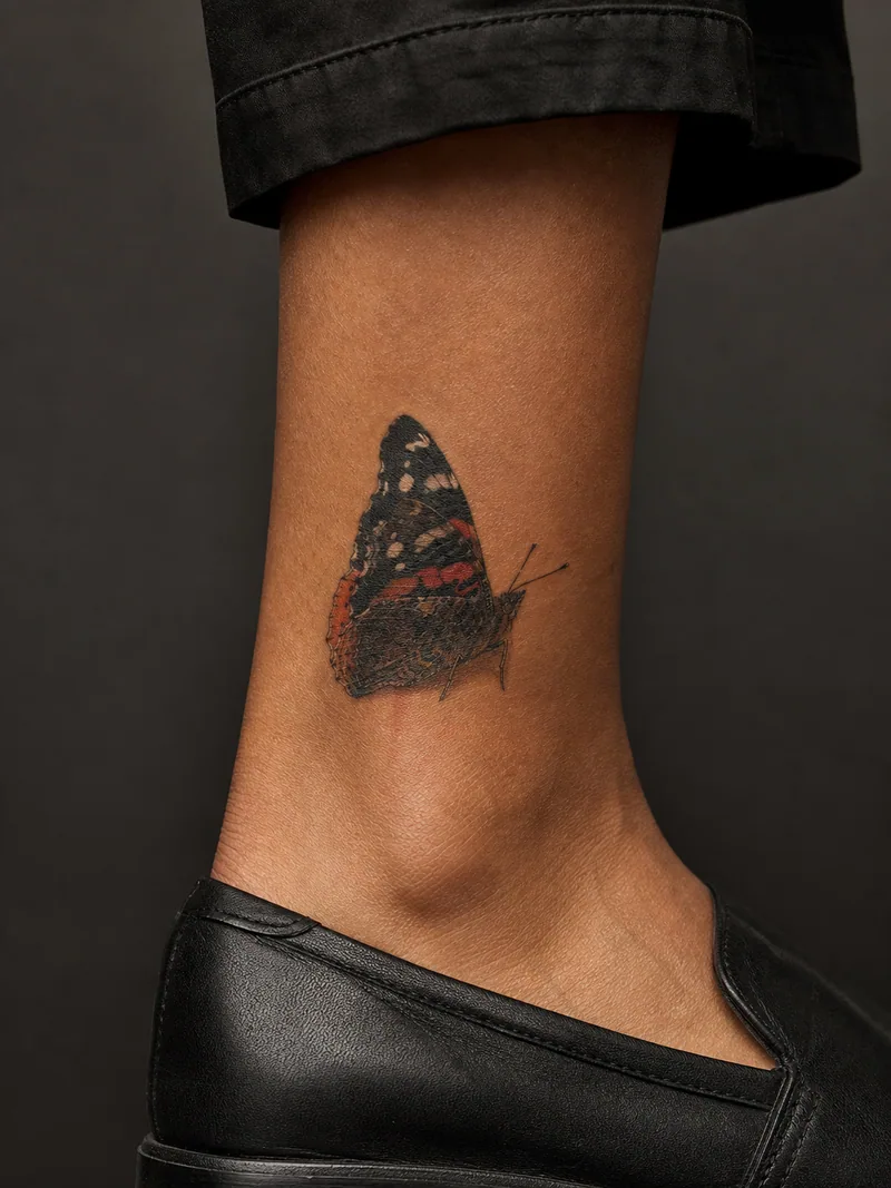 Red admiral tattoo - A red admiral rests with partly closed wings above the ankle.