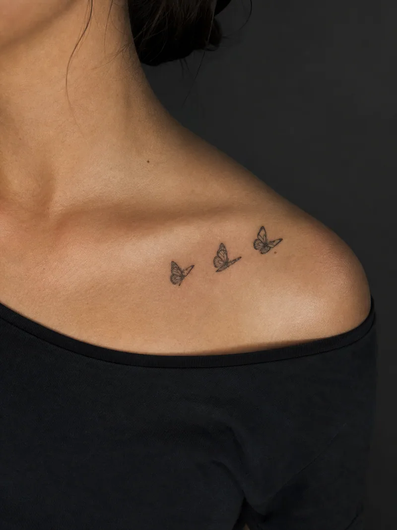 Three butterfly tattoo - Three outlined butterflies follow the collarbone in different flight angles.