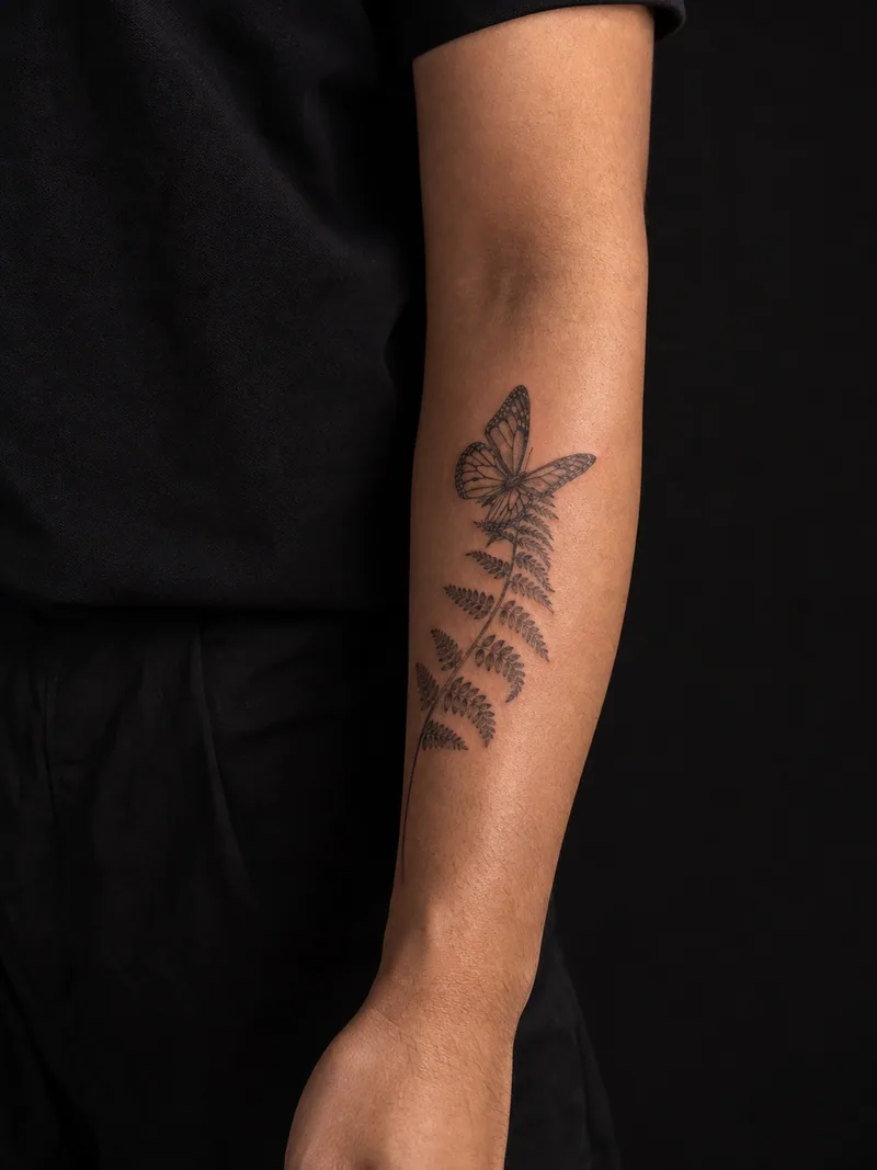Butterfly fern tattoo - A butterfly rests on a curved fern frond with botanical detail.