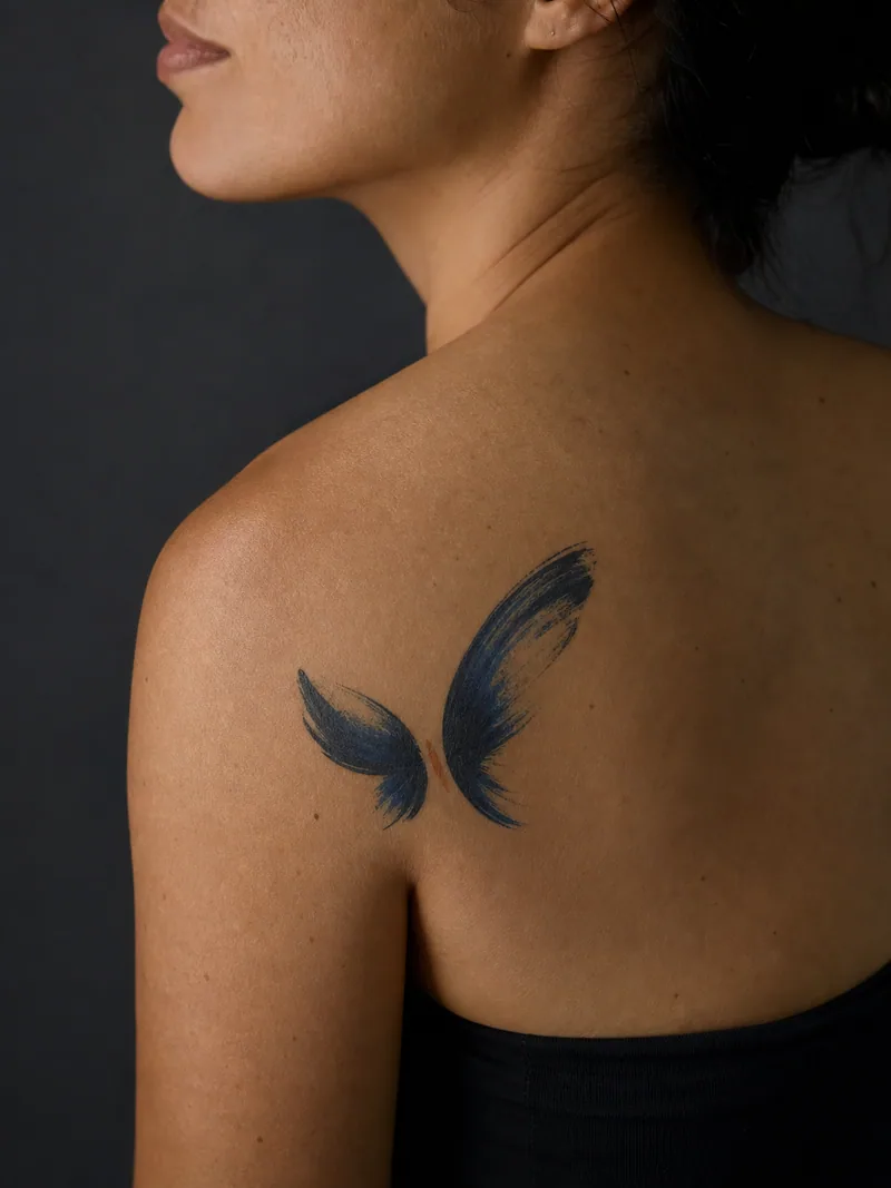 Abstract butterfly tattoo - Two brush gestures suggest wings around a small rust body mark.
