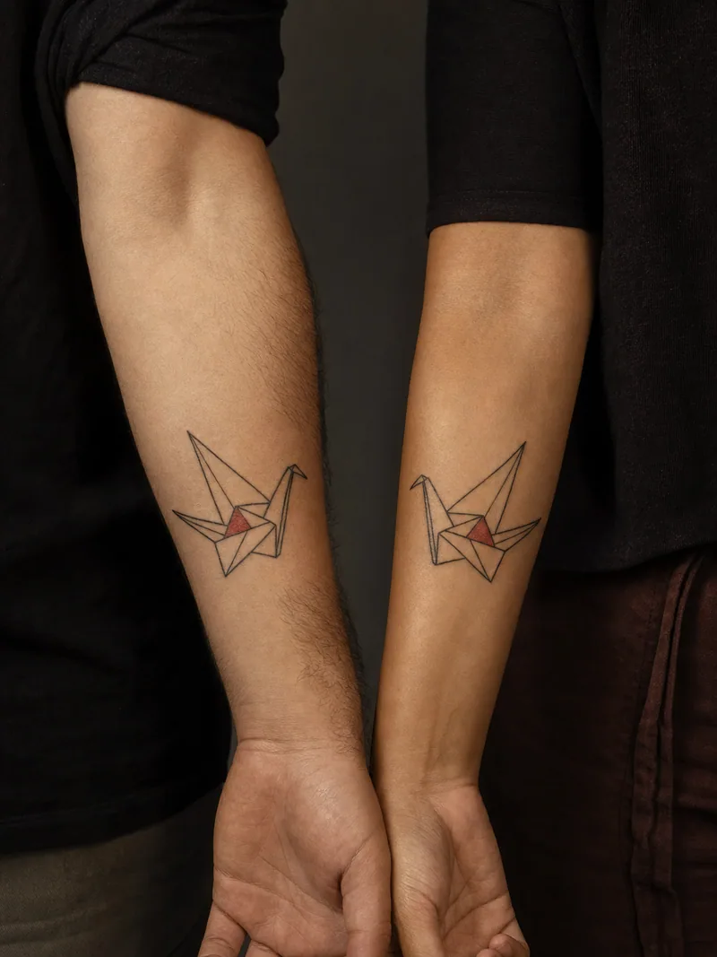 Origami crane couple tattoos - Mirrored paper cranes face each other with one red fold apiece.