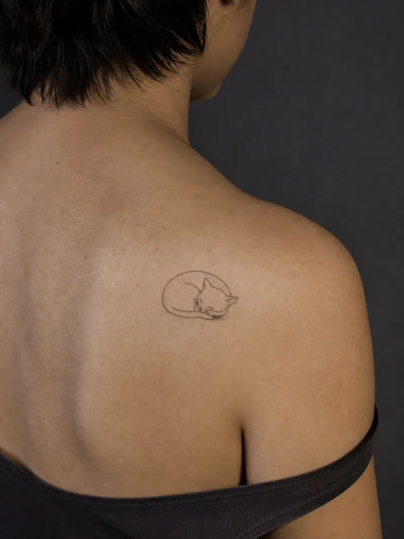 Fine-line cat tattoo - A curled sleeping cat uses one main contour and a small shadow.