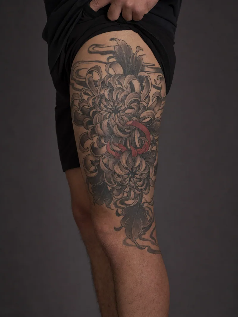 Japanese chrysanthemum tattoo - Layered chrysanthemum petals wrap the thigh through wind bars and one red accent.