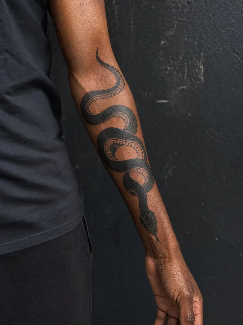 Blackwork snake tattoo - bold snake wrapping along a man's outer forearm