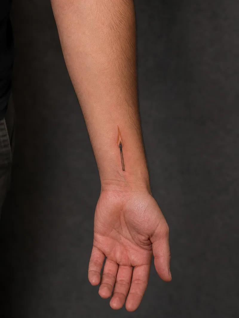 Tiny match forearm tattoo - A small burning match shows how a compact idea sits near the wrist.