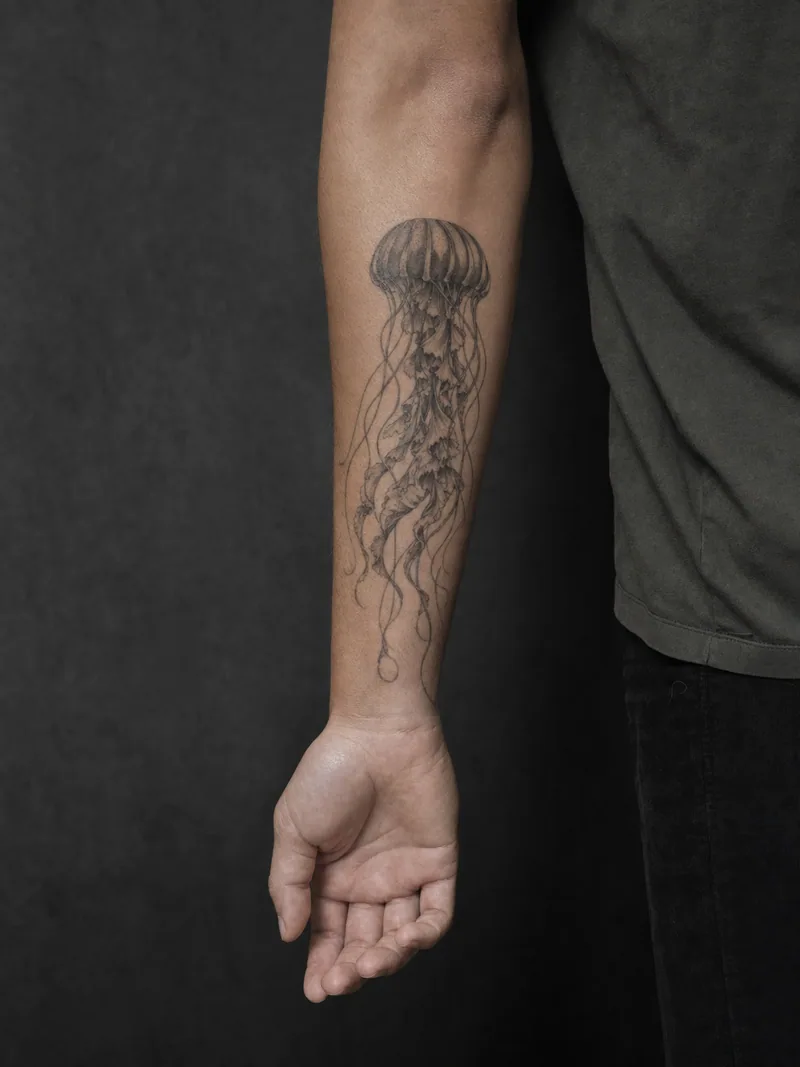 Jellyfish forearm tattoo - A translucent-looking jellyfish drifts vertically toward the wrist.