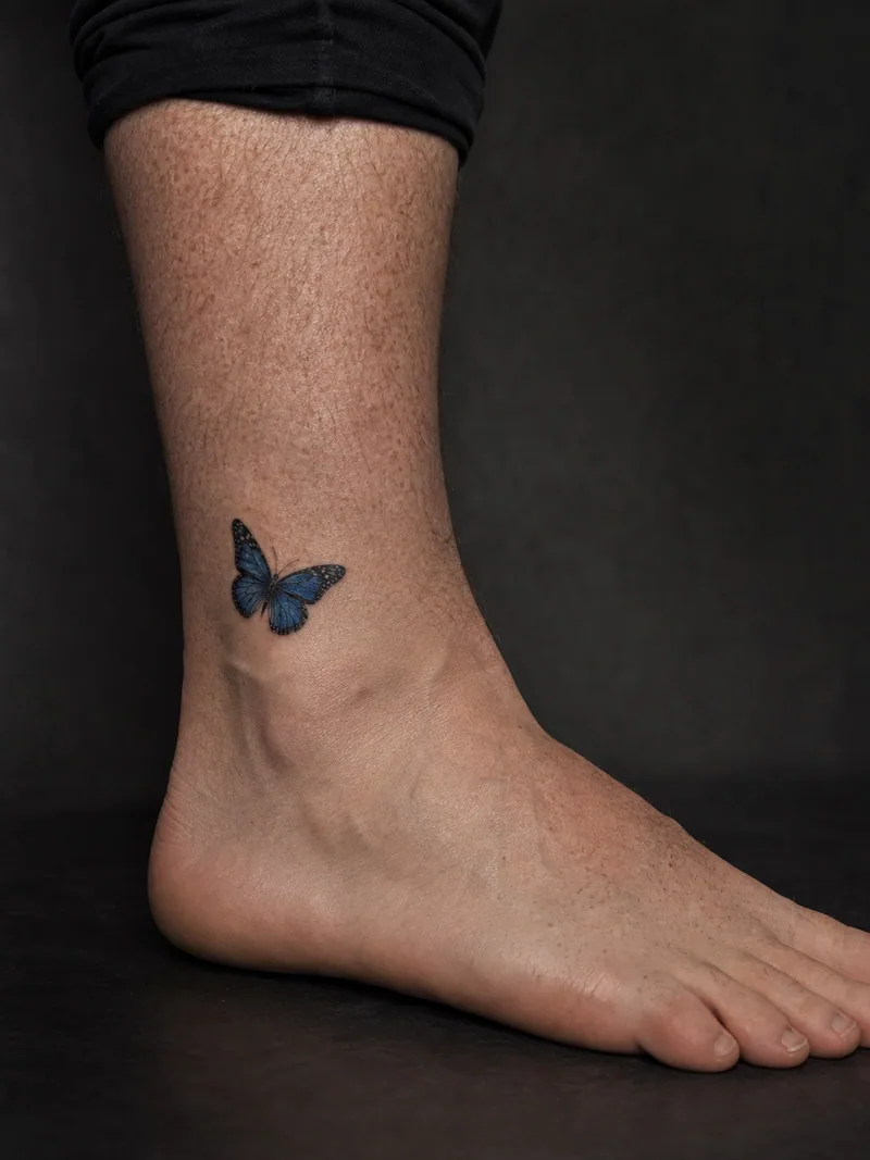 Blue butterfly ankle tattoo - small realistic blue butterfly placed with generous open skin