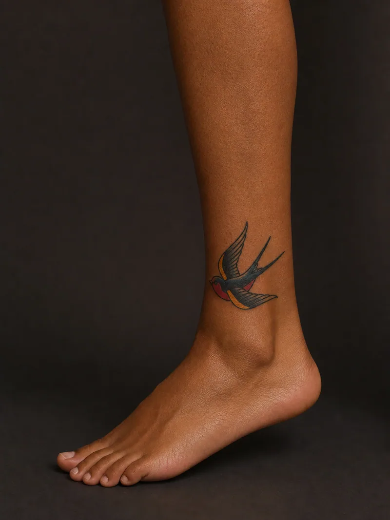 Swallow ankle tattoo - classic swallow in flight with a bold outline and balanced colour