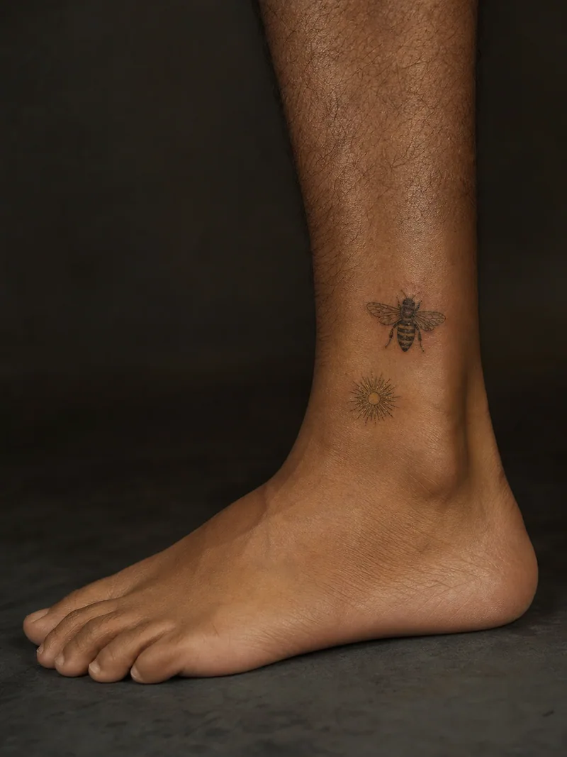 Bee ankle tattoo - small honey bee paired with a separate fine sunburst below it