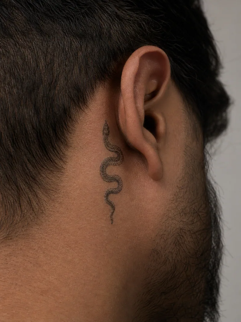 Snake behind ear tattoo - miniature scaled snake winding vertically in a compact S curve