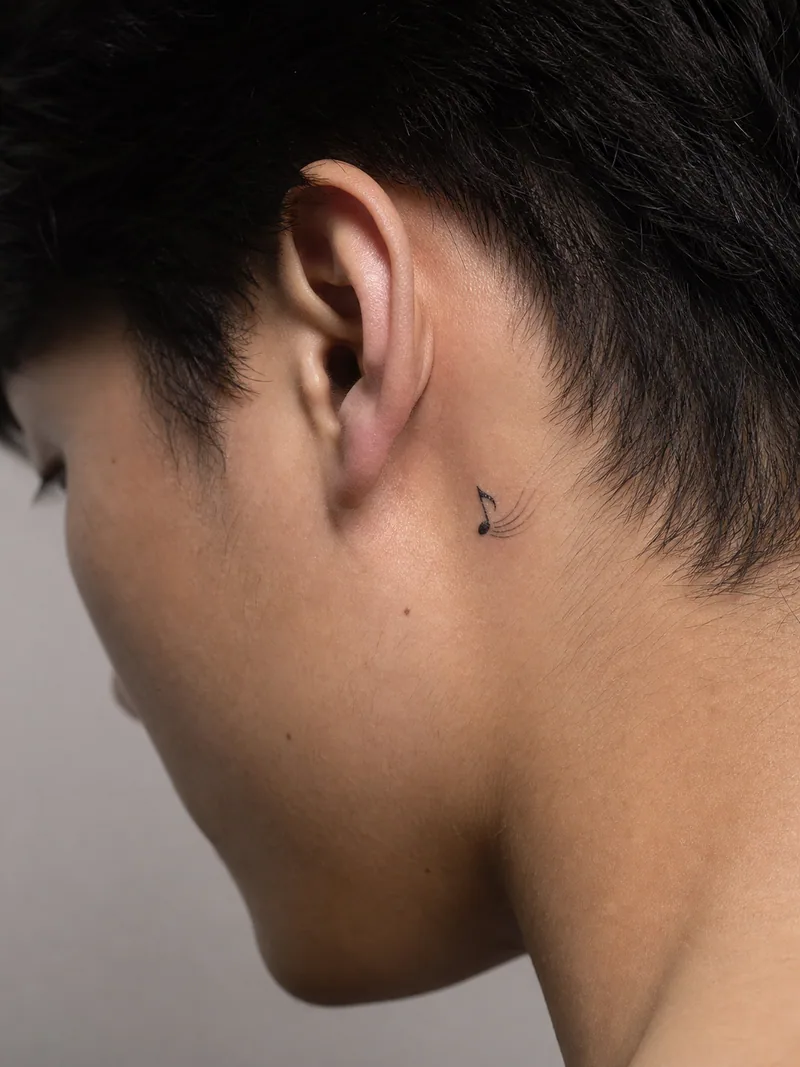Music note behind ear tattoo - single musical note paired with a subtle curved sound line