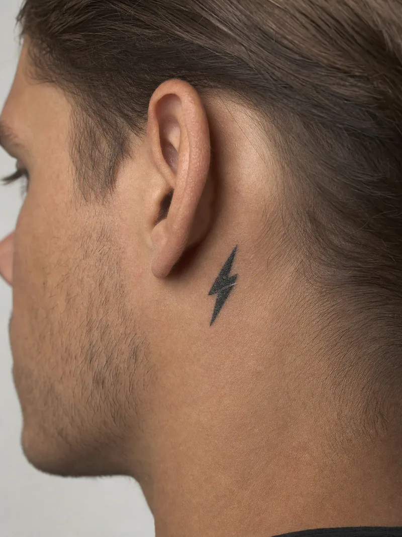 Lightning behind ear tattoo - bold miniature lightning bolt with one clean negative-space cut