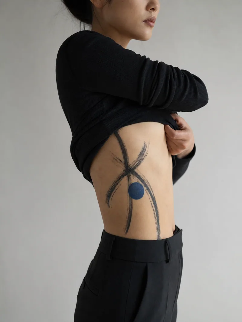 Abstract rib tattoo - sweeping black brushstrokes crossing one restrained blue circle