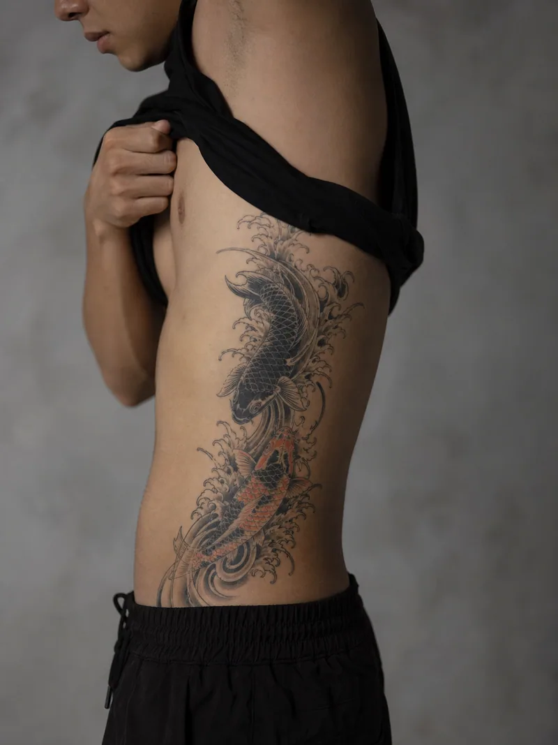 Koi rib tattoo - two koi fish moving vertically through layered waves