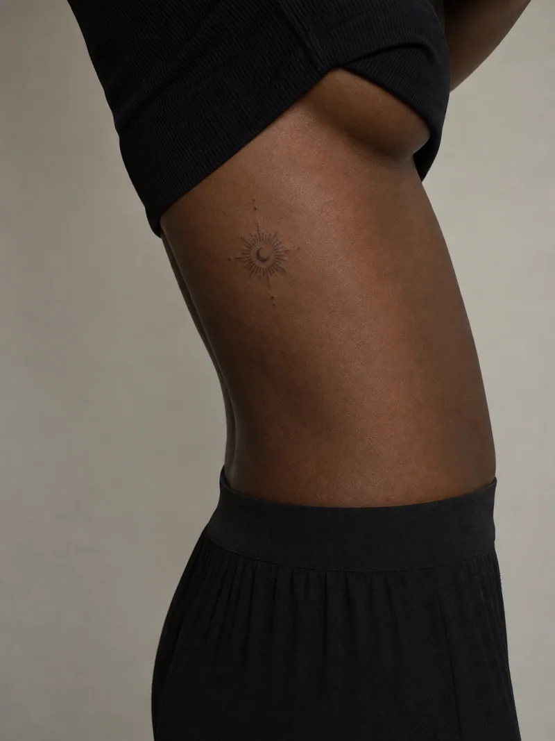 Small sun rib tattoo - radiant sun with a tiny crescent and sparse vertical dots