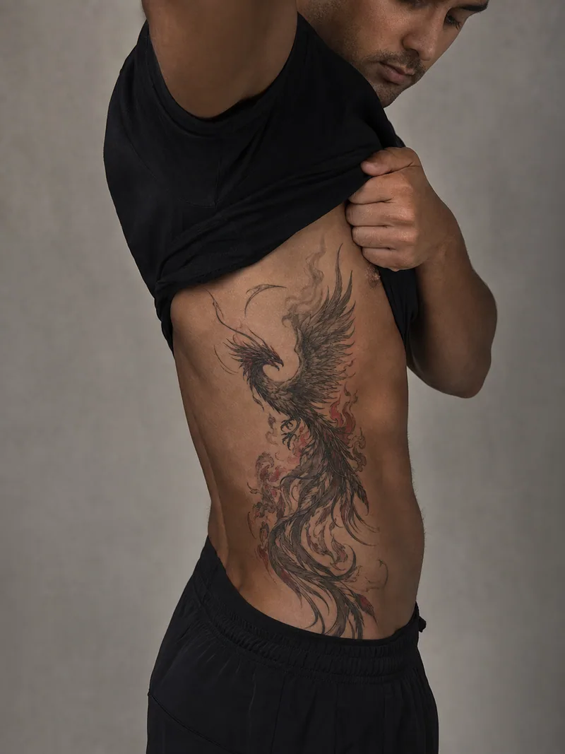 Phoenix rib tattoo - rising phoenix with flowing feathers and restrained ember-red accents