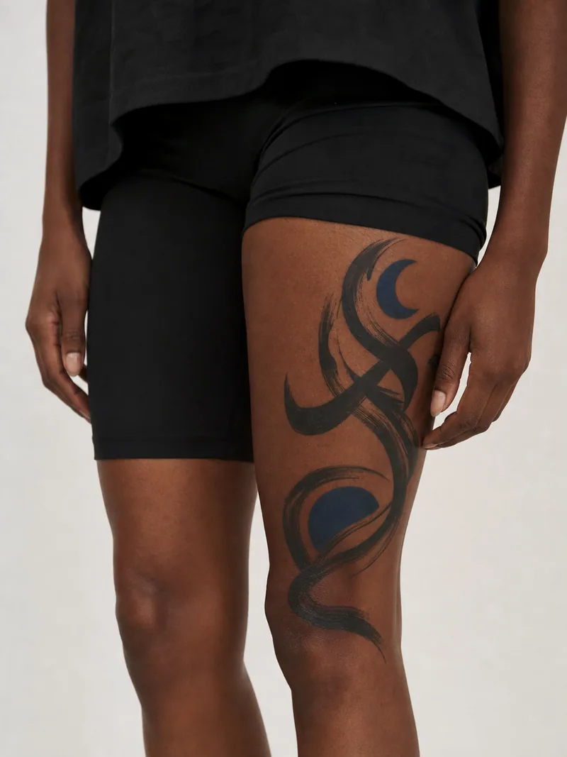 Abstract thigh tattoo - sweeping brush ribbons with two restrained cobalt-blue shapes and skin breaks