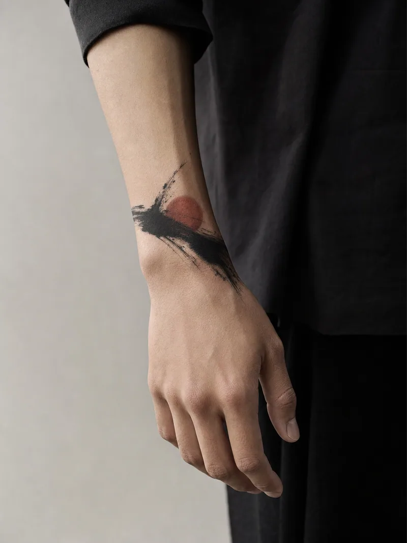 Abstract brushwork wrist tattoo - expressive black brushstroke crossing one restrained rust-red circle