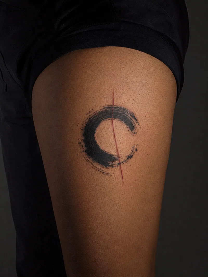 Abstract brush tattoo - a circular dry-brush gesture crossed by one restrained red line