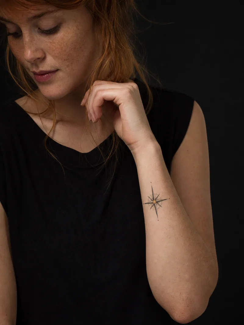 Small compass tattoo - precise compass rose with one restrained gold dot and no labels