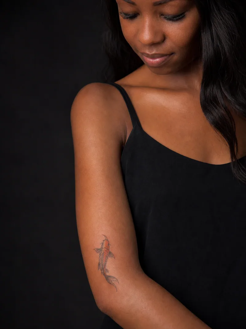 Small koi tattoo - small orange koi swimming upward along the forearm