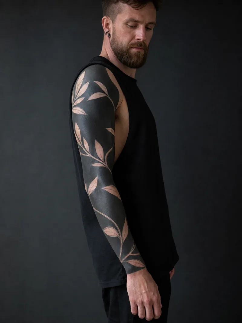 Negative-space blackout sleeve - Solid black fields frame broad botanical windows of untouched skin.