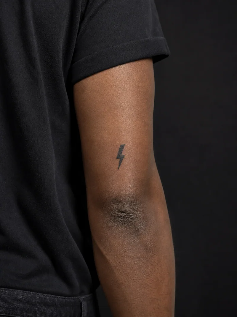 Lightning bolt tattoo - A single sharp bolt creates a high-contrast mark above the elbow.