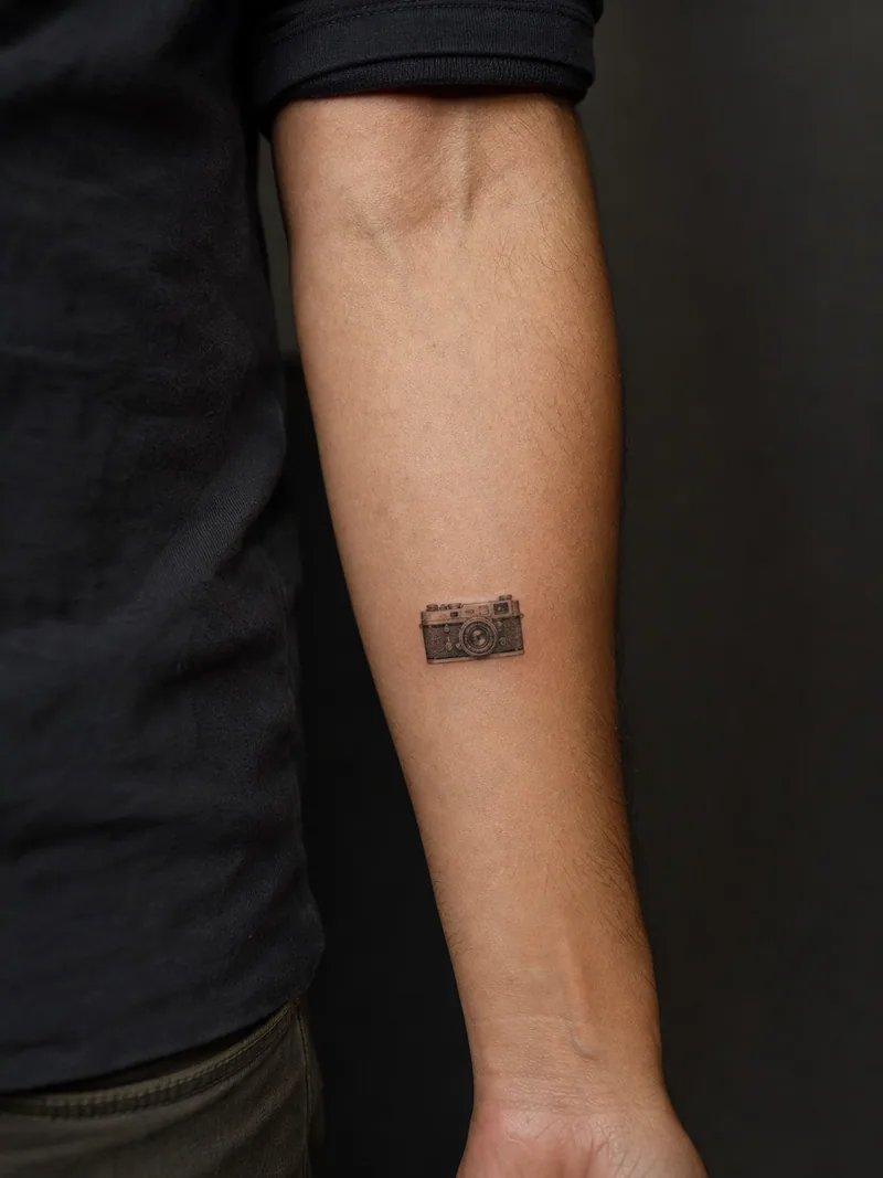 Vintage camera tattoo - A tiny rangefinder camera keeps recognizable controls without brand text.