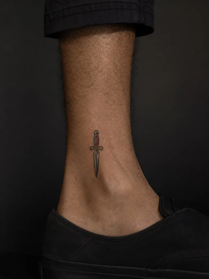 Small dagger tattoo - A short dagger uses a bold outline and a muted red handle for clarity.