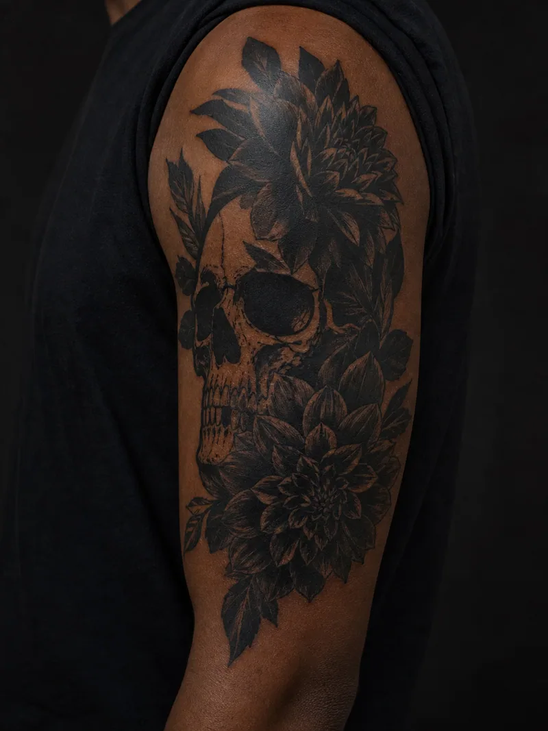 Skull and dahlias tattoo - a non-graphic skull emerging from dense black dahlia blooms