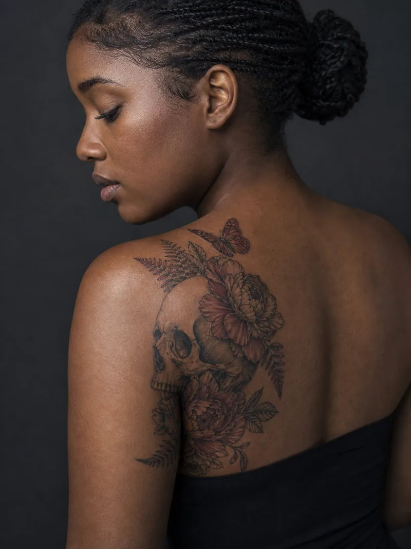 Floral skull tattoo - elegant skull profile softened by peonies, ferns and a butterfly