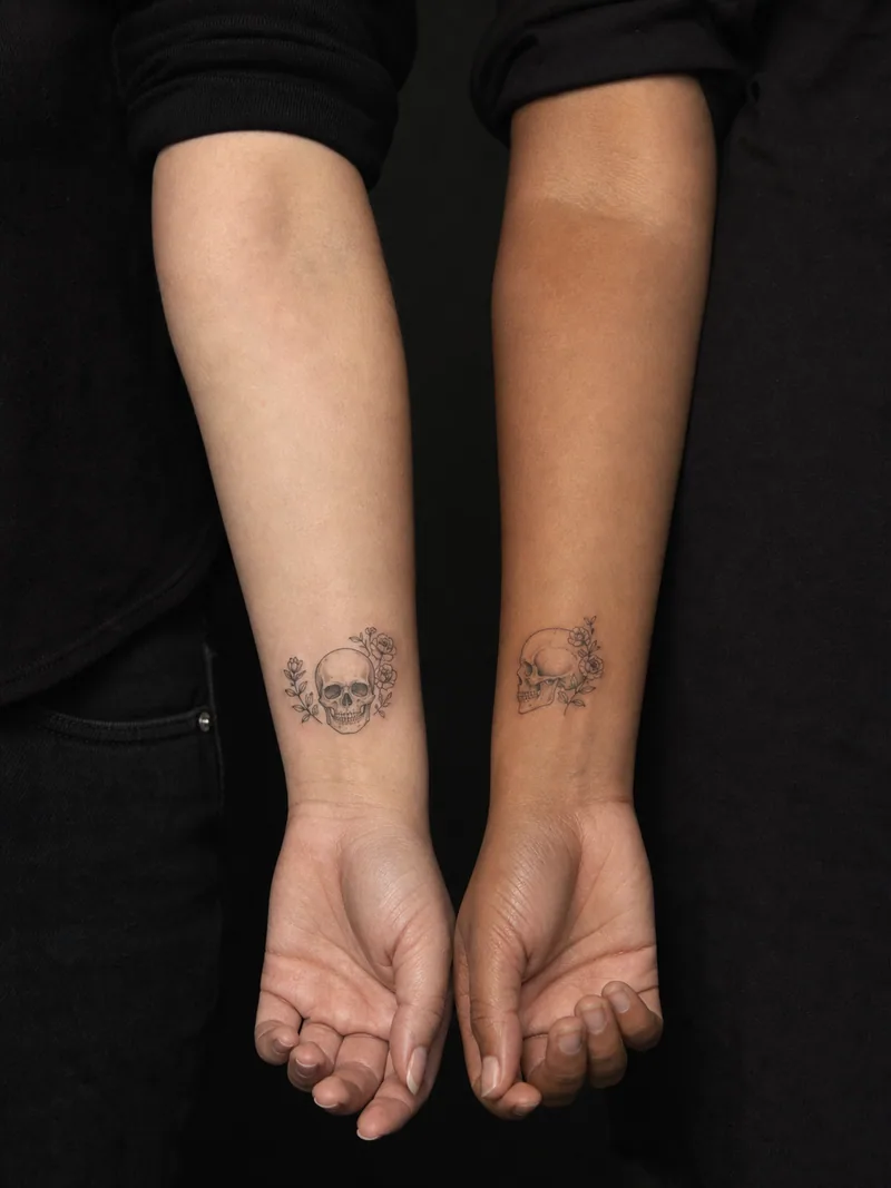 Matching skull tattoos - complementary front and side-profile skulls with tiny flowers