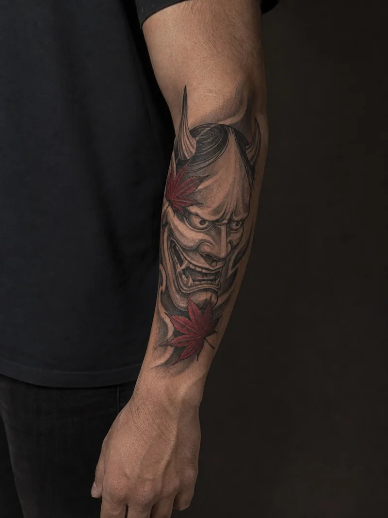Hannya mask tattoo - A hannya mask anchors a vertical layout with two red maple leaves.