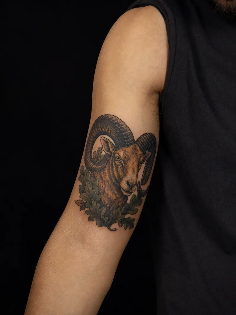 Ram bicep tattoo - Curved horns frame a ram portrait and green oak leaves.
